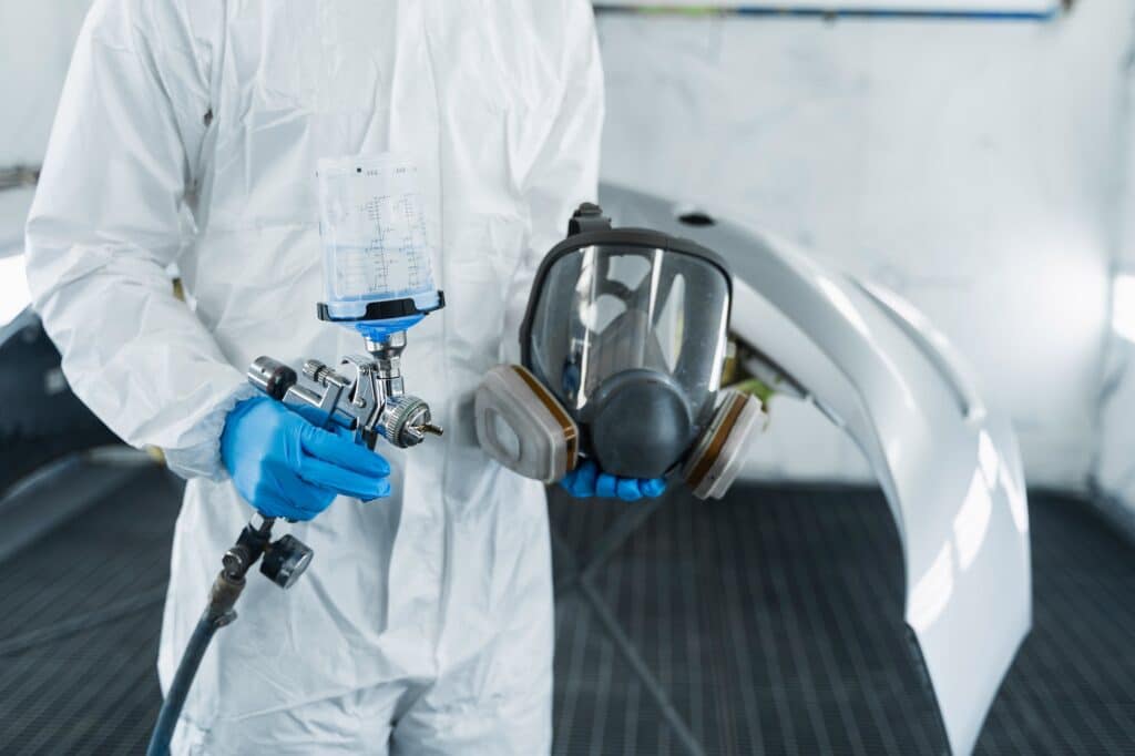 Сlose-up view of car painter with paint gun and protective respirator in hands.